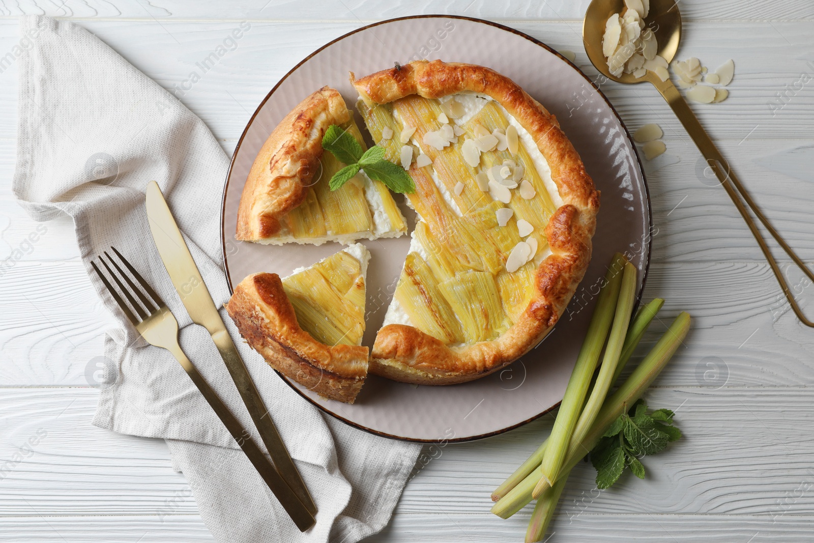 Photo of Freshly baked rhubarb pie, stalks, almond flakes and cutlery on white wooden table, flat lay