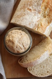 Photo of Sourdough starter in glass jar and bread on wooden table, top view