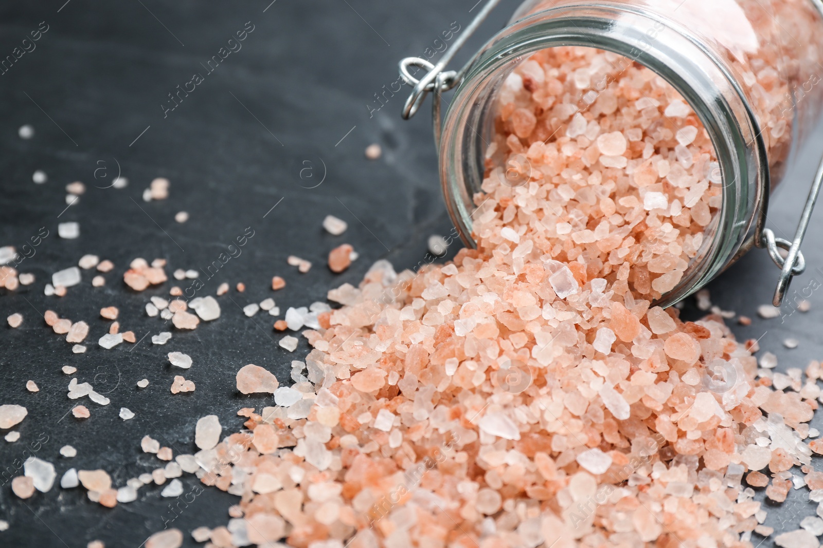 Photo of Overturned glass jar with pink himalayan salt on black table, closeup