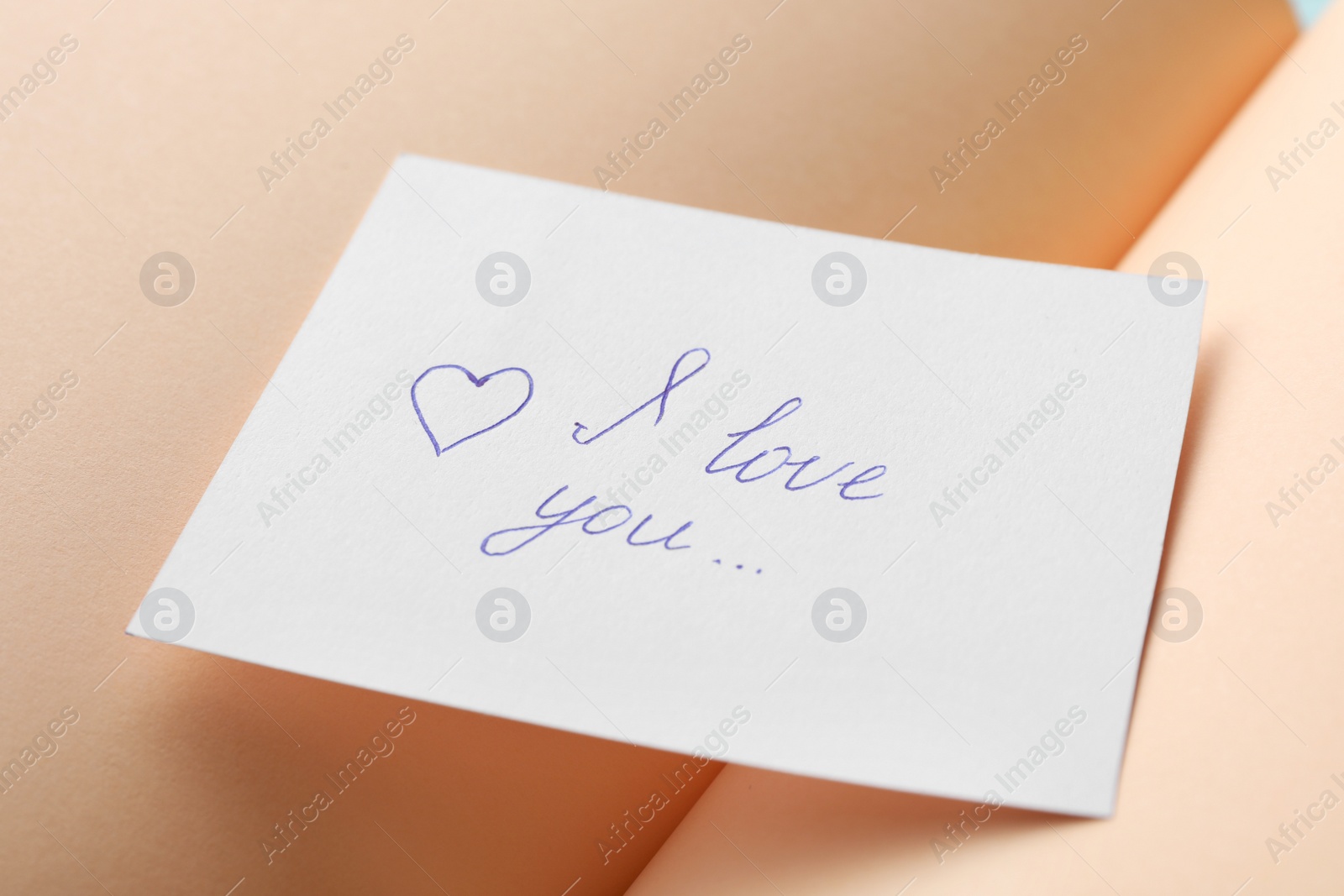 Photo of Paper sheet with words I LOVE YOU on open notebook, closeup