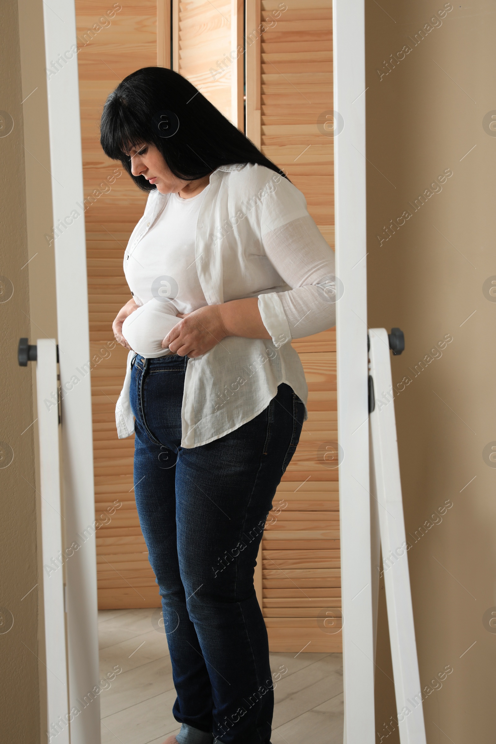 Photo of Overweight woman in tight shirt near mirror at home