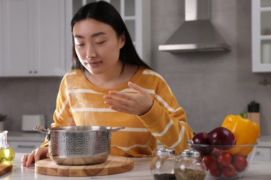 Photo of Beautiful woman smelling soup after cooking at countertop in kitchen