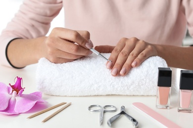 Photo of Woman removing fingernail cuticles at table, closeup. At-home manicure