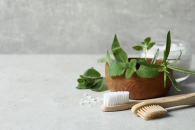 Toothbrushes, sea salt and green herbs on light grey table, closeup. Space for text