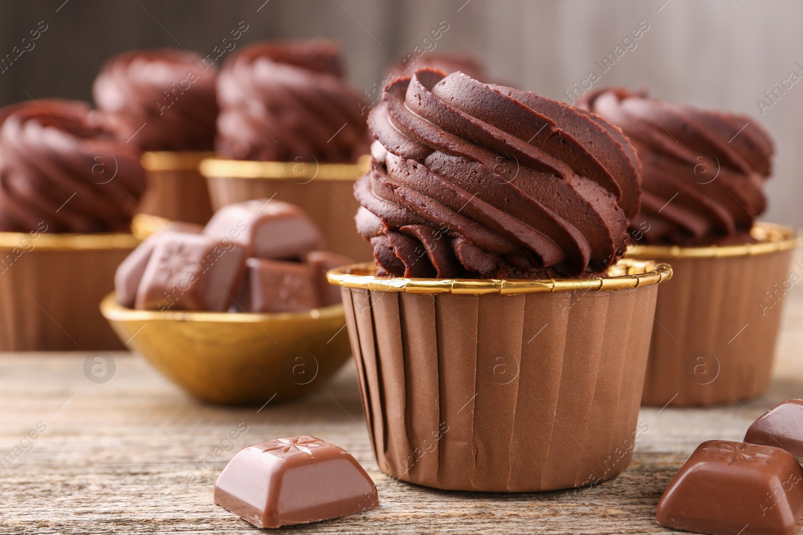 Photo of Delicious cupcakes and chocolate pieces on wooden table, closeup