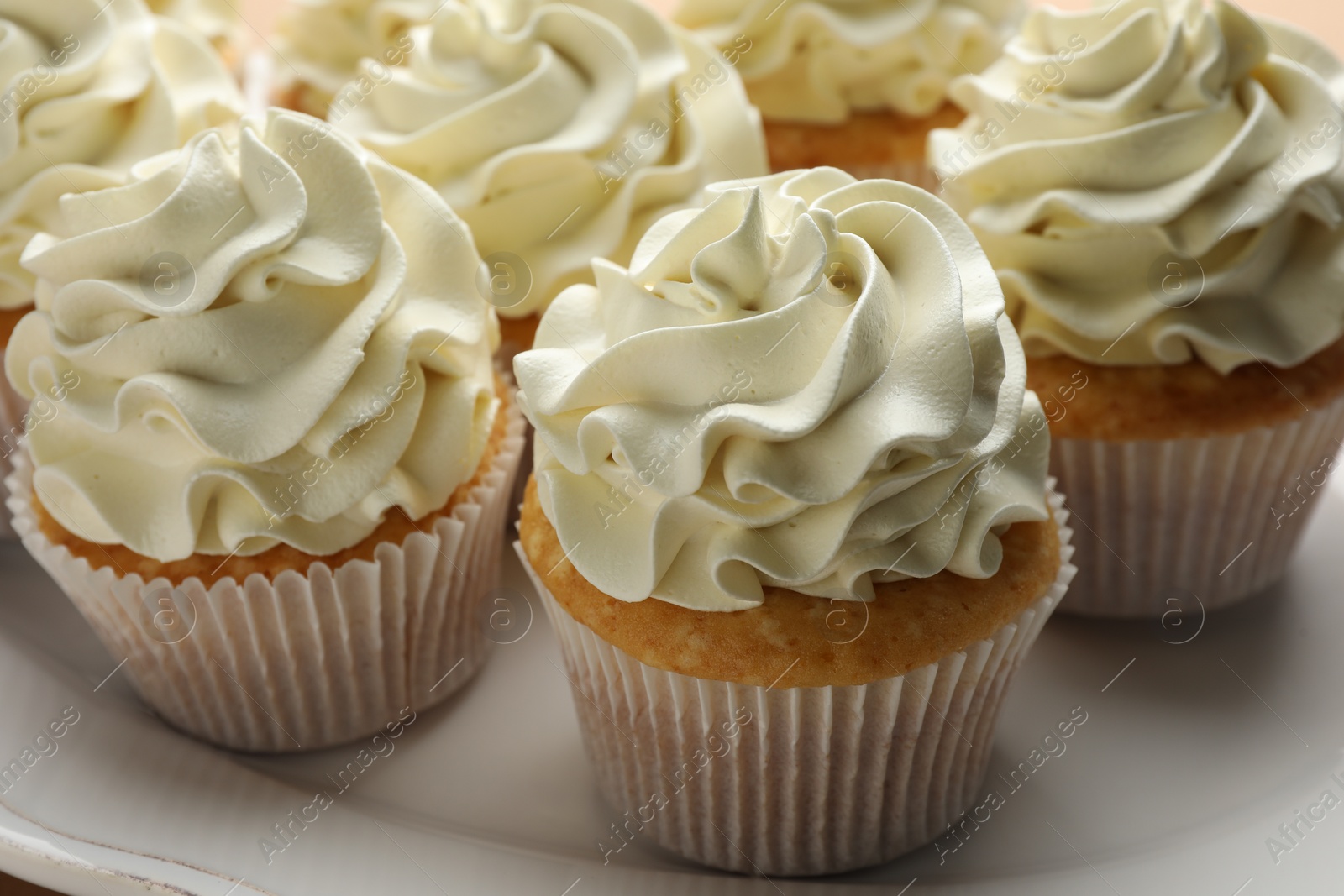 Photo of Tasty vanilla cupcakes with cream on plate, closeup