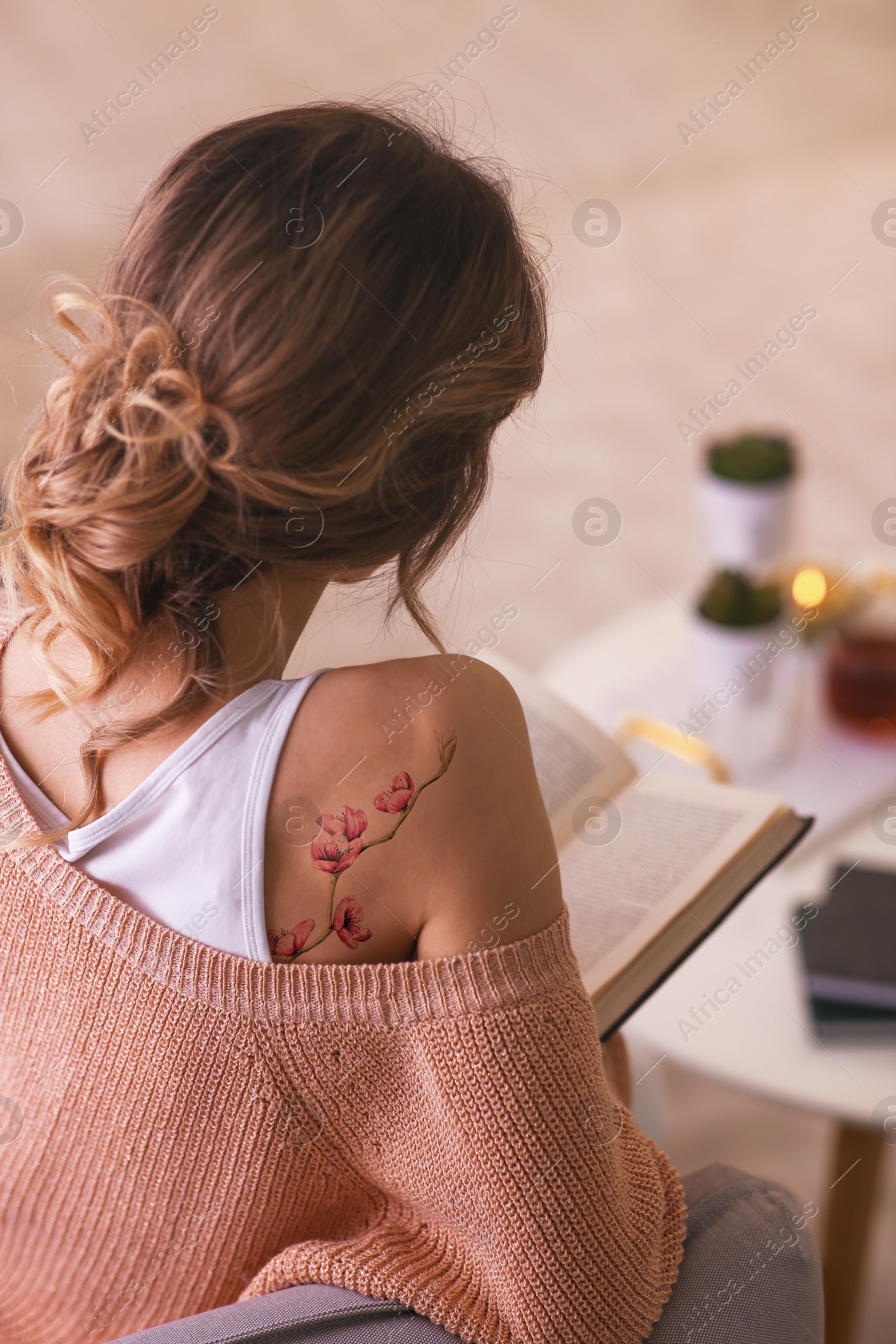 Image of Young woman with tattoo of beautiful sakura tree branch reading at home, back view