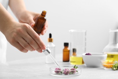 Scientist developing cosmetic oil at light grey table, closeup