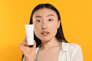 Photo of Beautiful young woman holding sun protection cream on orange background