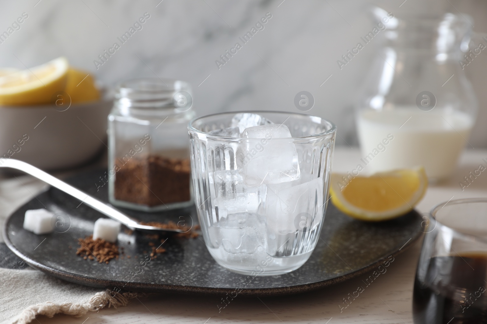 Photo of Cooking iced coffee. Ice cubes in glass, ingredients and spoon on white wooden table, closeup