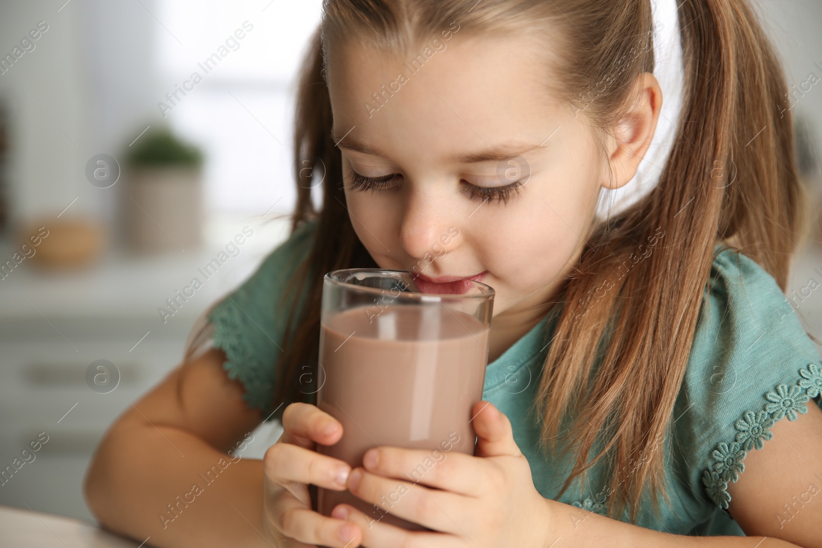 Photo of Cute little child drinking tasty chocolate milk in kitchen, closeup