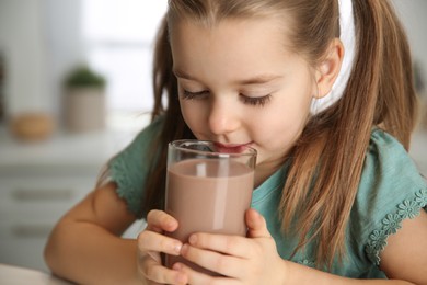 Photo of Cute little child drinking tasty chocolate milk in kitchen, closeup