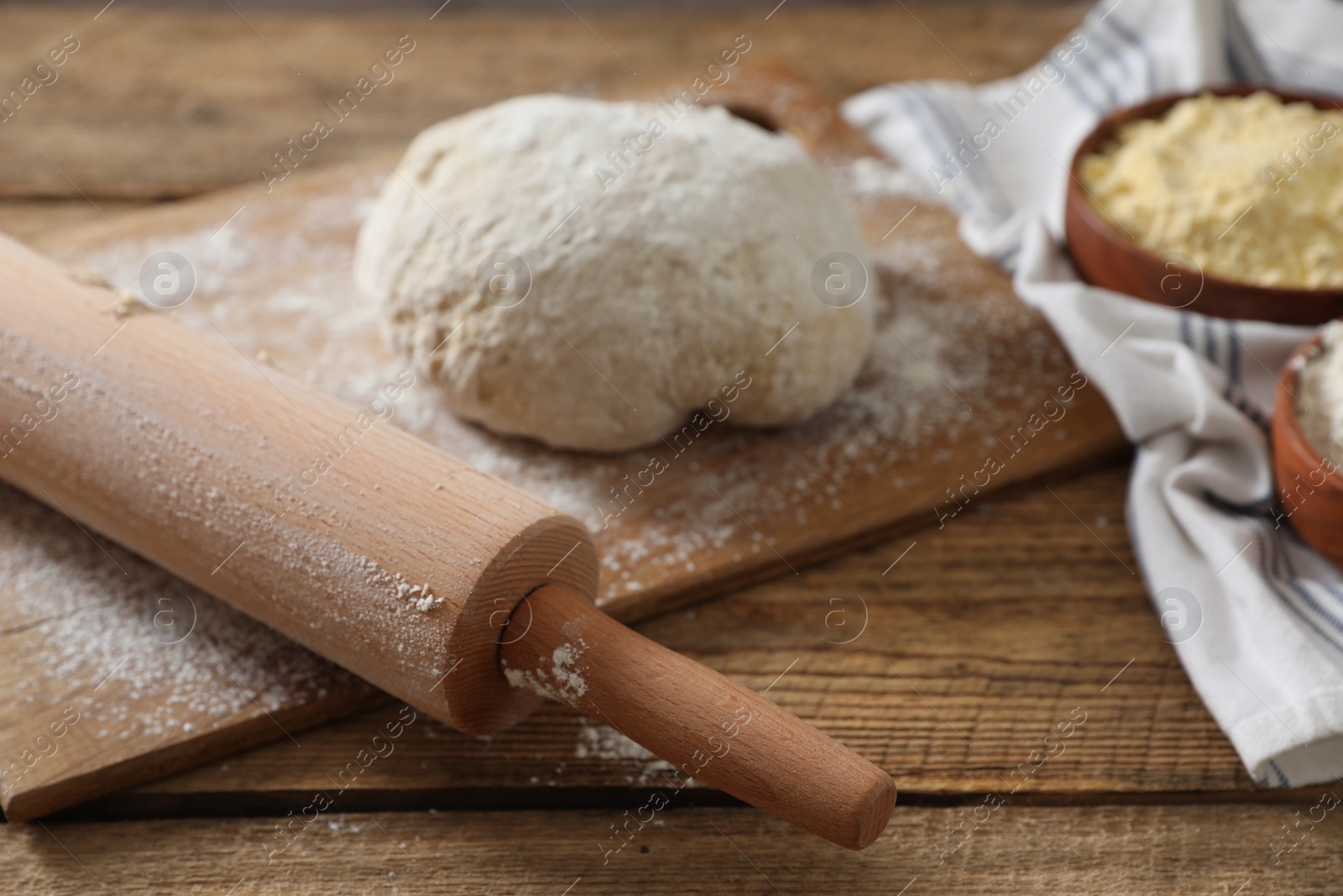 Photo of Rolling pin, flour and dough on wooden table, closeup
