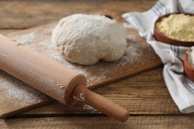 Photo of Rolling pin, flour and dough on wooden table, closeup