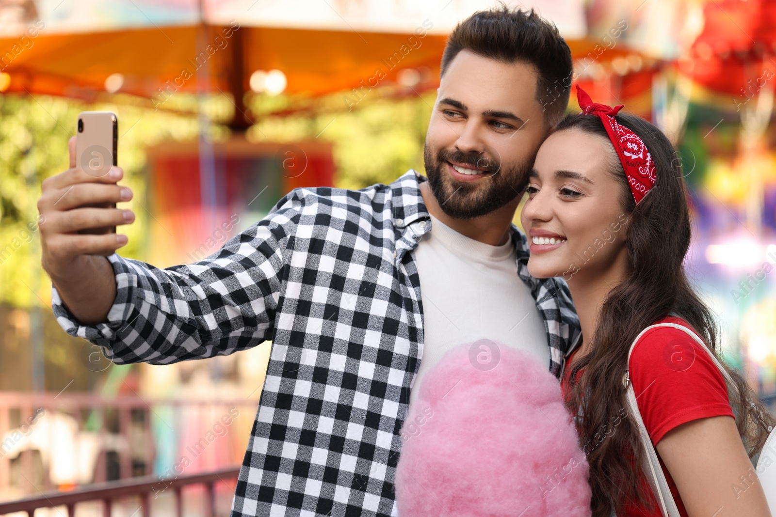 Photo of Happy young man and his girlfriend with cotton candy taking selfie at funfair