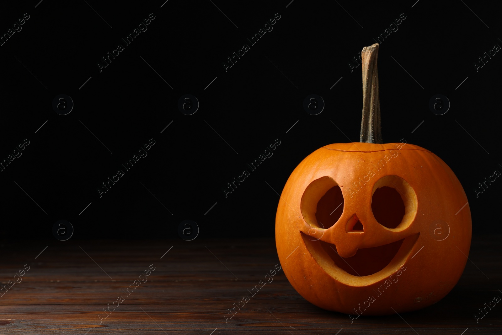 Photo of Scary jack o'lantern made of pumpkin on wooden table in darkness, space for text. Halloween traditional decor