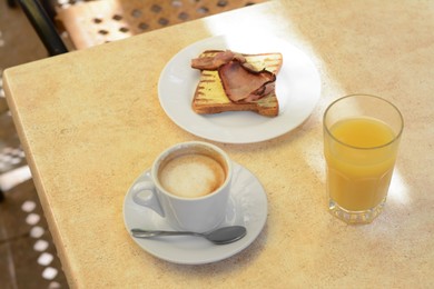 Photo of Cup of coffee and delicious sandwich with fried bacon on beige table