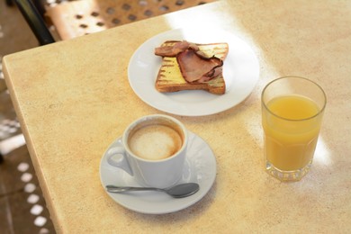 Cup of coffee and delicious sandwich with fried bacon on beige table