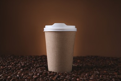 Coffee to go. Paper cup on roasted beans against brown background