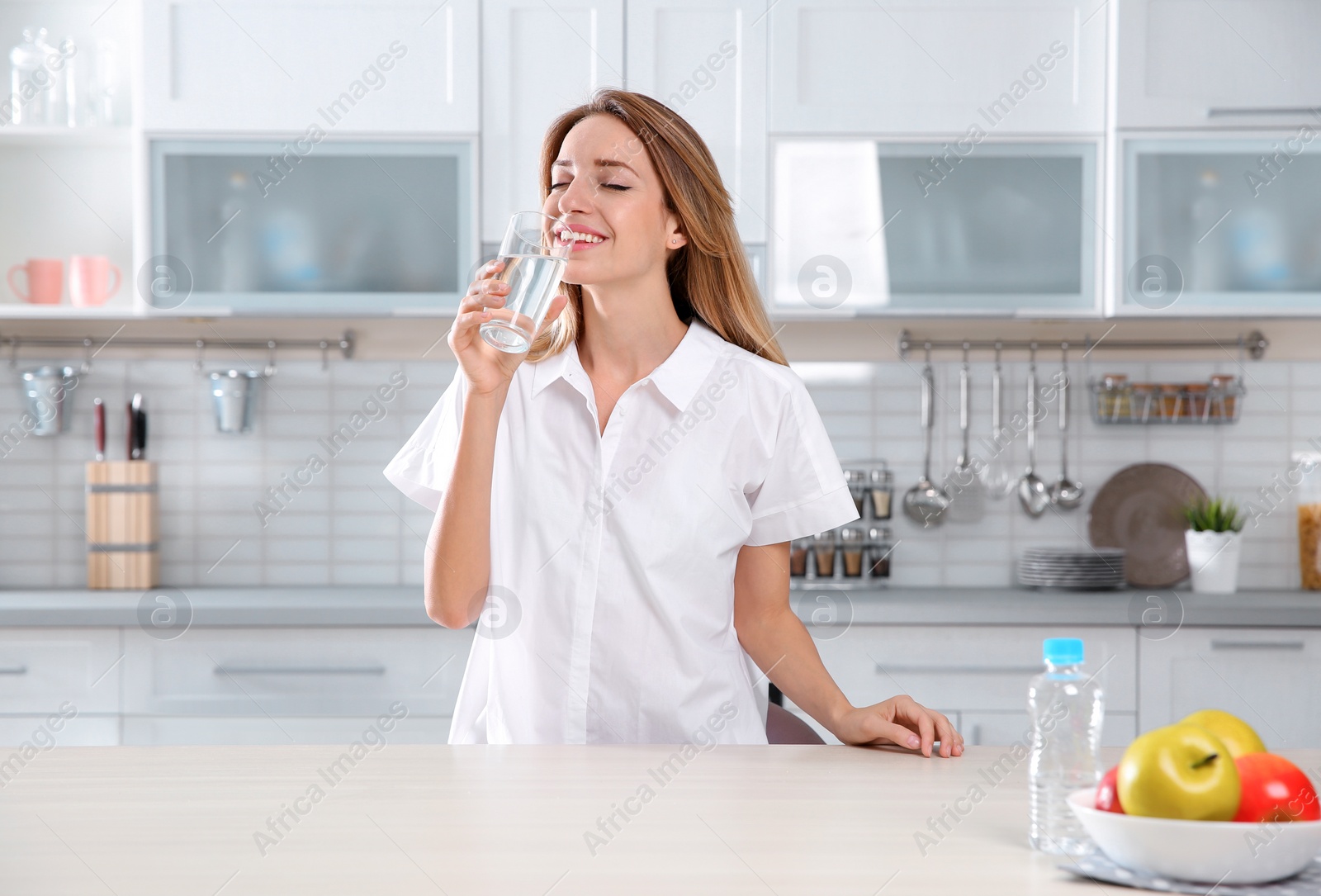 Photo of Young woman drinking clean water from glass in kitchen