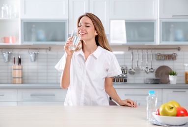 Photo of Young woman drinking clean water from glass in kitchen