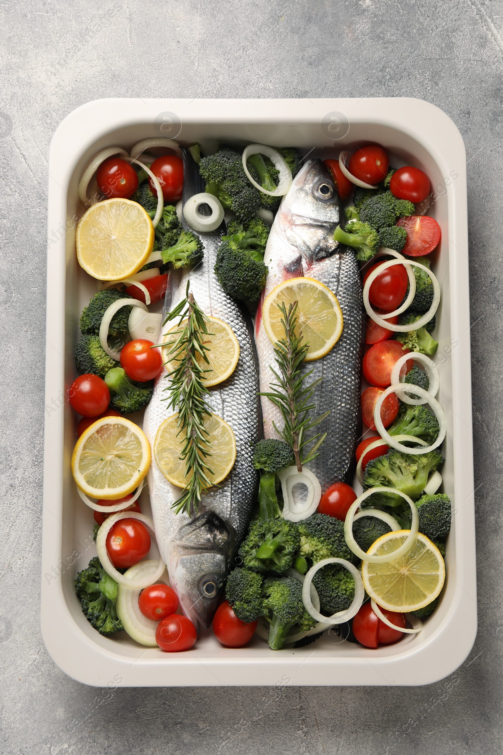 Photo of Raw fish with vegetables and lemon in baking dish on grey textured table, top view