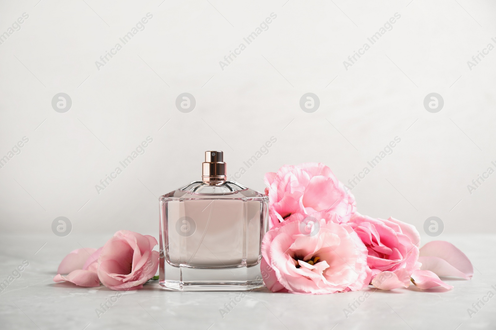Photo of Bottle of perfume with fresh flowers on light background
