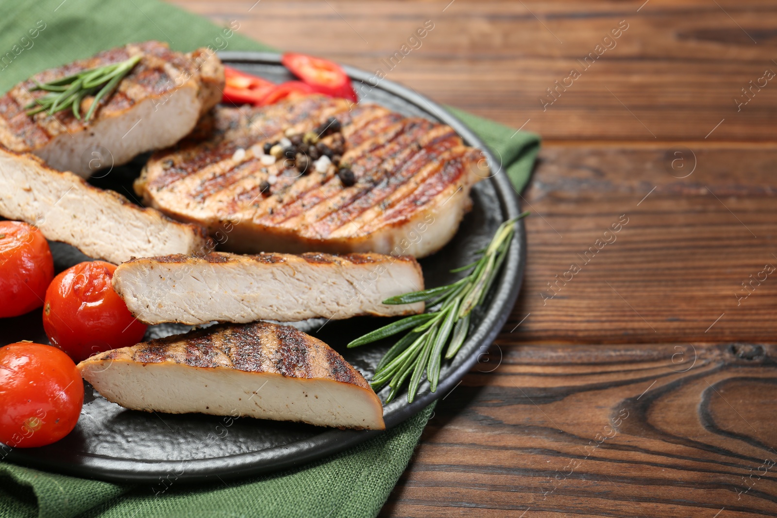 Photo of Grilled pork steaks with rosemary, spices and tomatoes on wooden table. Space for text