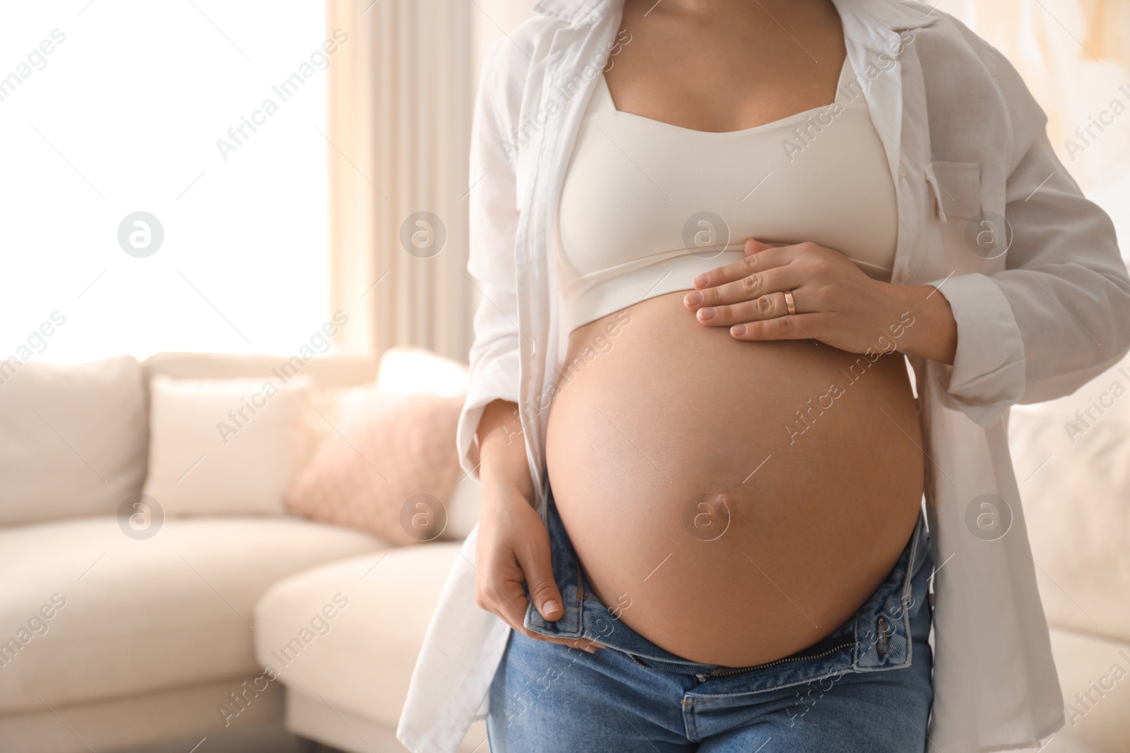 Photo of Pregnant young woman touching belly at home, closeup. Space for text