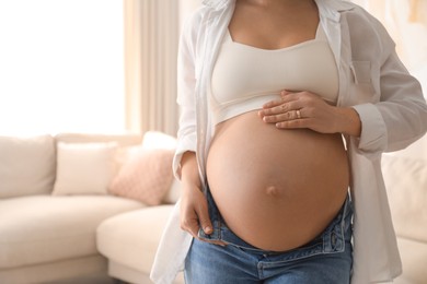 Pregnant young woman touching belly at home, closeup. Space for text