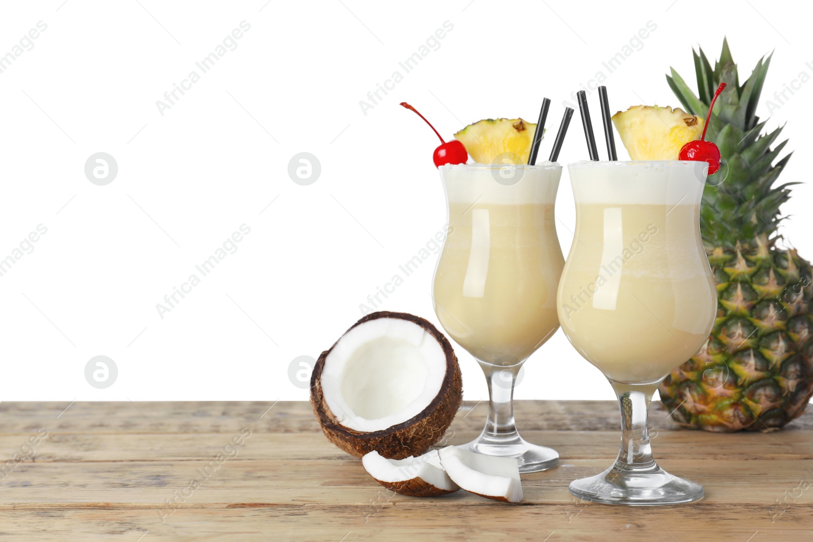 Photo of Tasty Pina Colada cocktail and ingredients on wooden table against white background, space for text