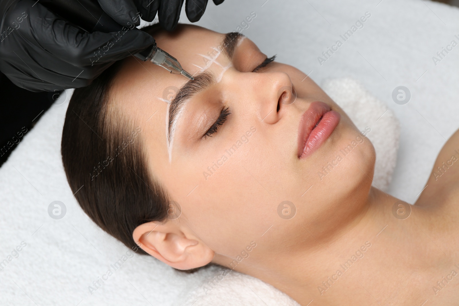 Photo of Beautician making permanent eyebrow makeup to young woman, closeup