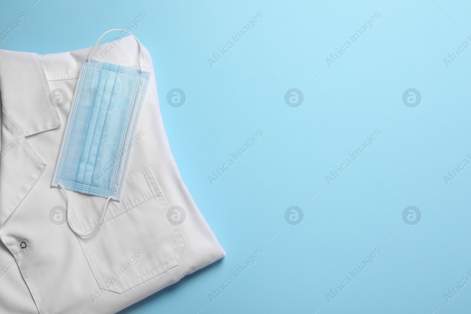 Photo of Medical uniform and face mask on light blue background, flat lay. Space for text