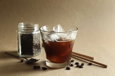 Refreshing iced coffee in glass, beans and straws on beige background, closeup