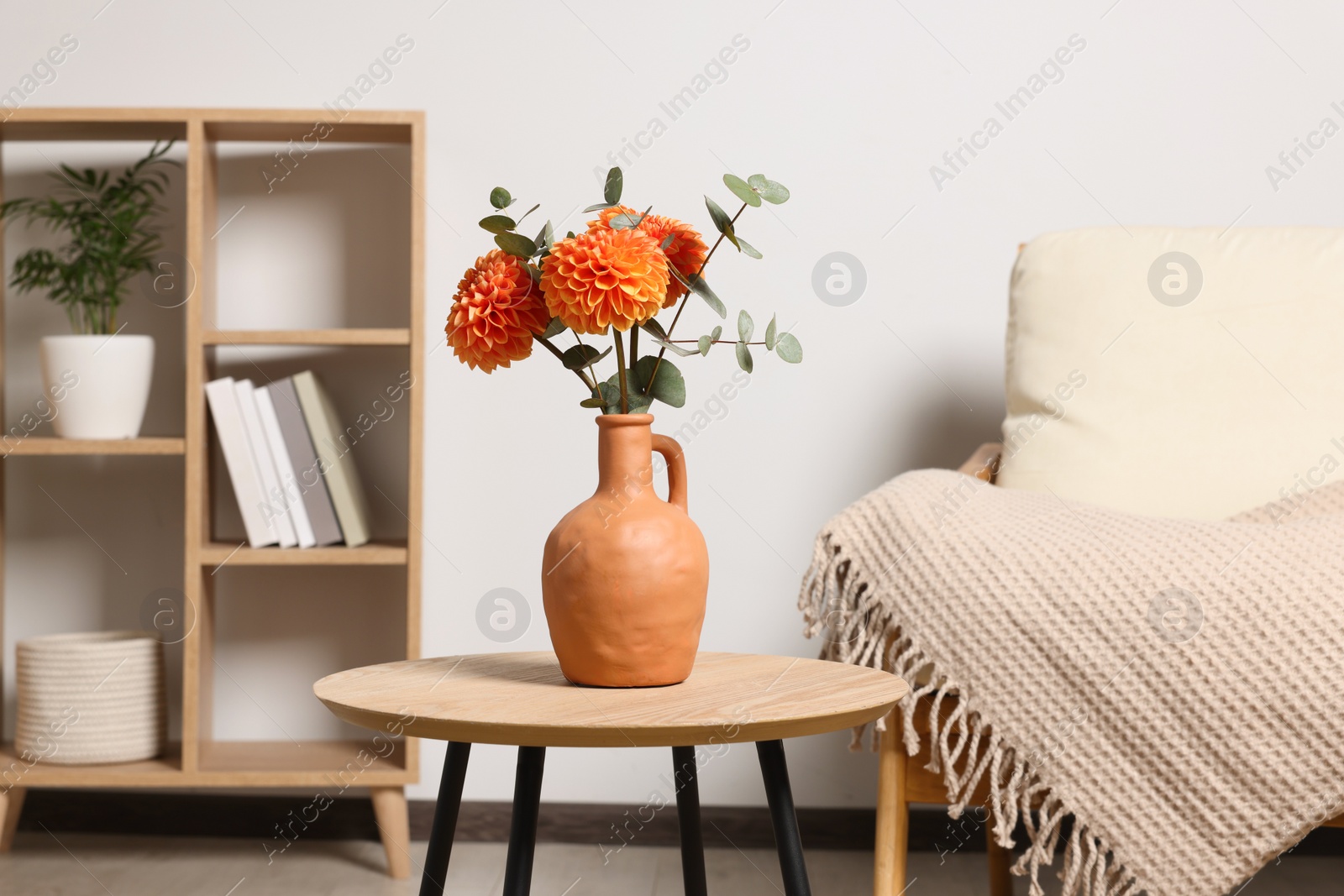 Photo of Ceramic vase with beautiful flowers on coffee table near armchair indoors