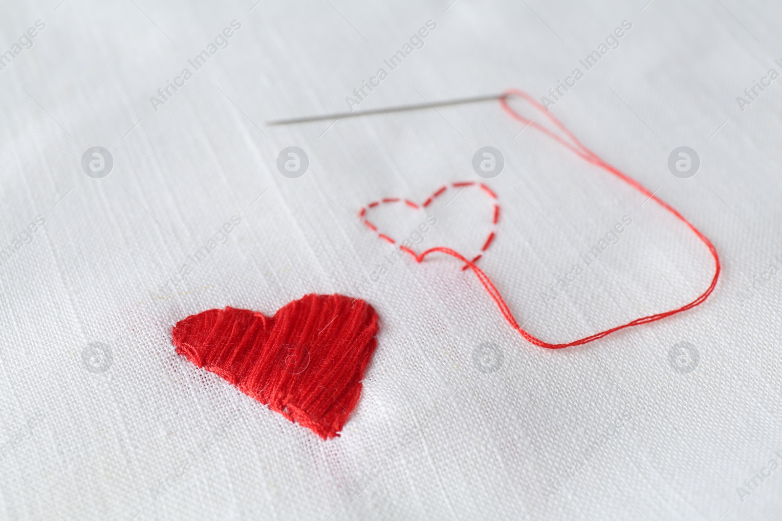 Photo of Embroidered red heart and needle on white cloth, closeup