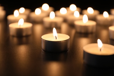 Photo of Burning candles on table in darkness, closeup. Funeral symbol