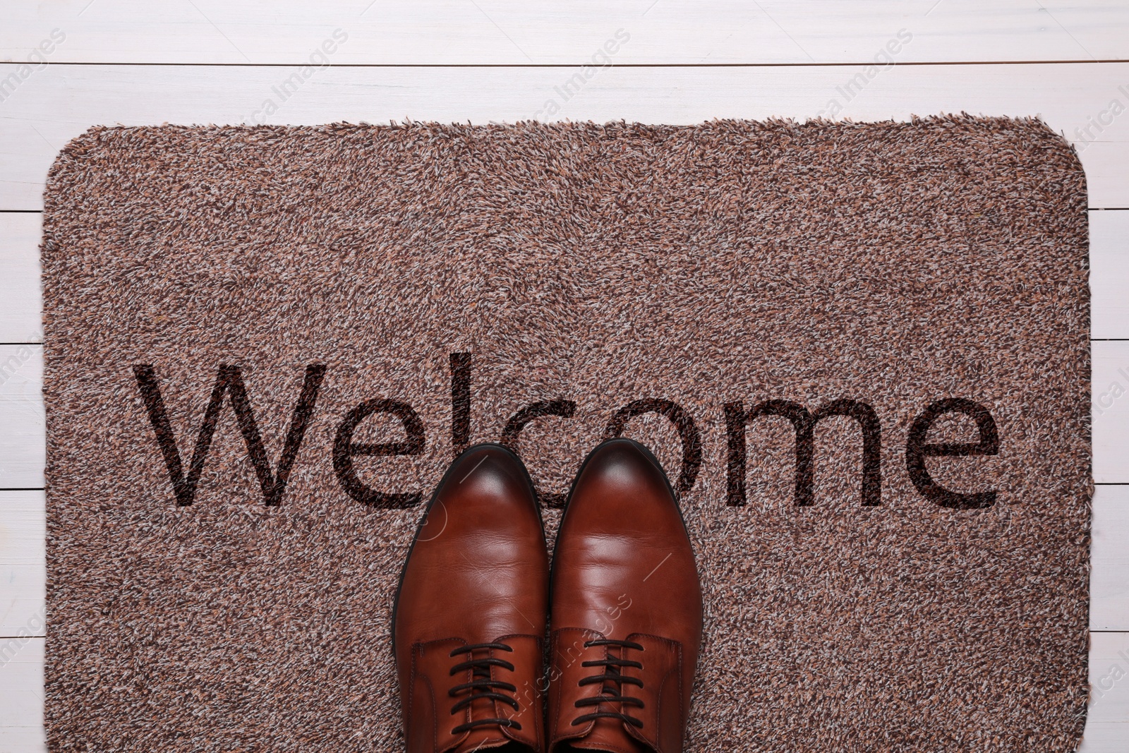 Image of Door mat with word WELCOME and shoes on white wooden floor, top view