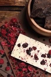 Different chocolate bars with freeze dried fruits on wooden table, flat lay