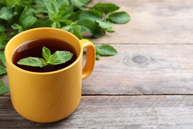 Cup with hot aromatic mint tea on wooden table, space for text