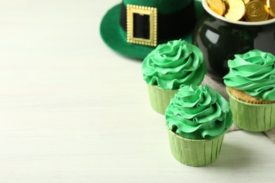St. Patrick's day party. Tasty cupcakes with green cream, pot of gold and leprechaun hat on white table, closeup. Space for text