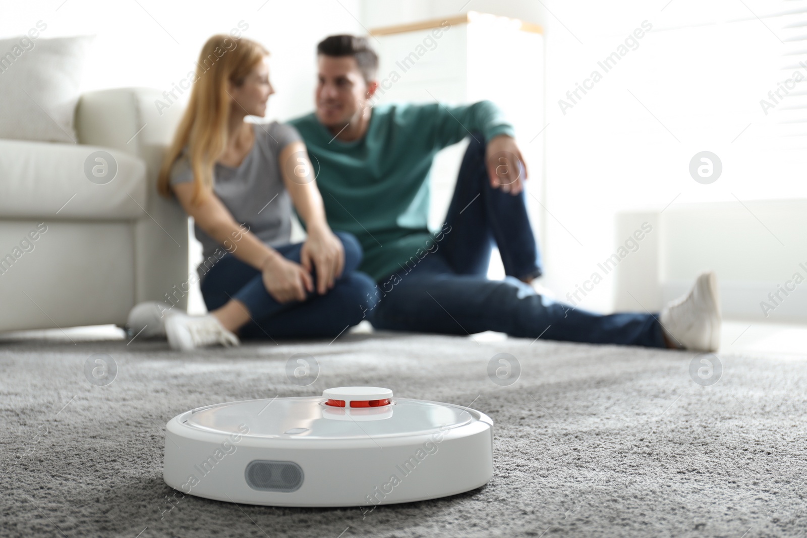 Photo of Couple spending time together while robotic vacuum cleaner doing its work at home