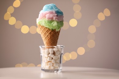 Photo of Sweet cotton candy in waffle cone on table against blurred lights, closeup