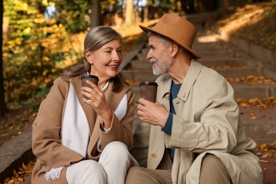 Photo of Affectionate senior couple with cups of coffee spending time together in autumn park