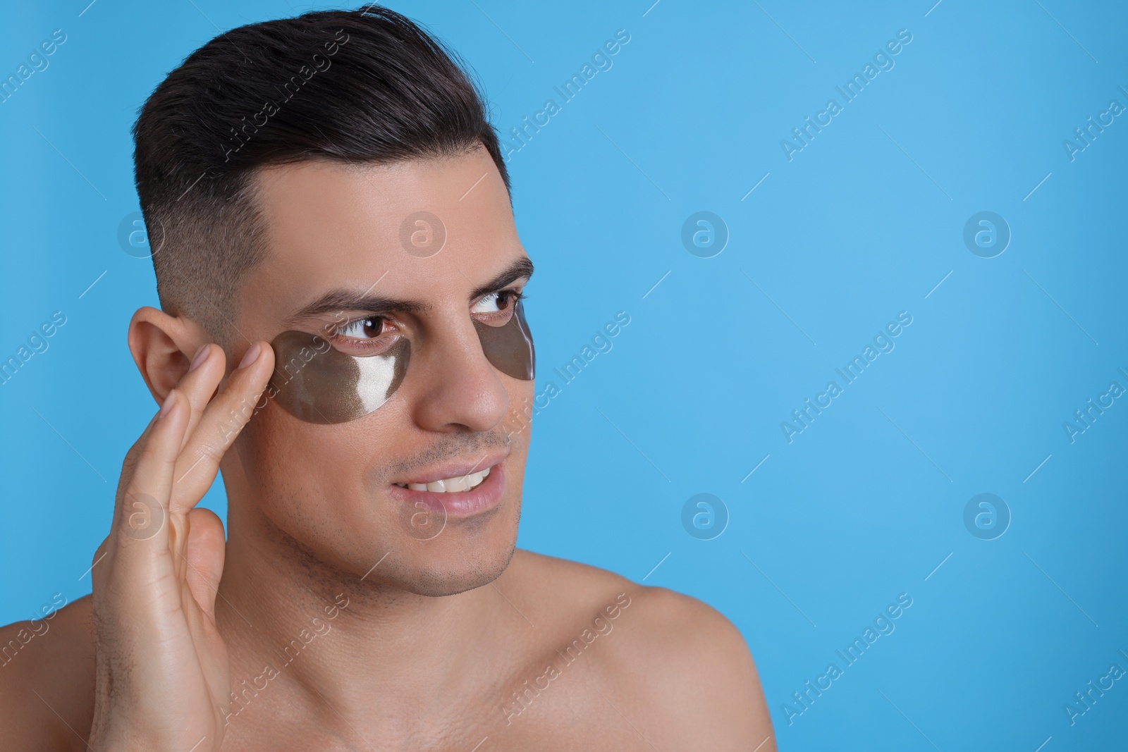 Photo of Man applying dark under eye patch on light blue background. Space for text