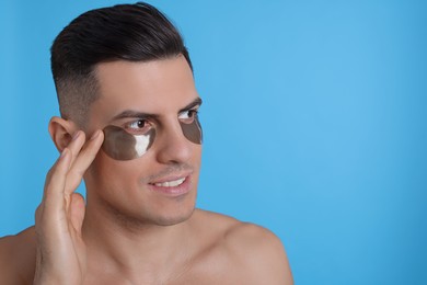 Man applying dark under eye patch on light blue background. Space for text