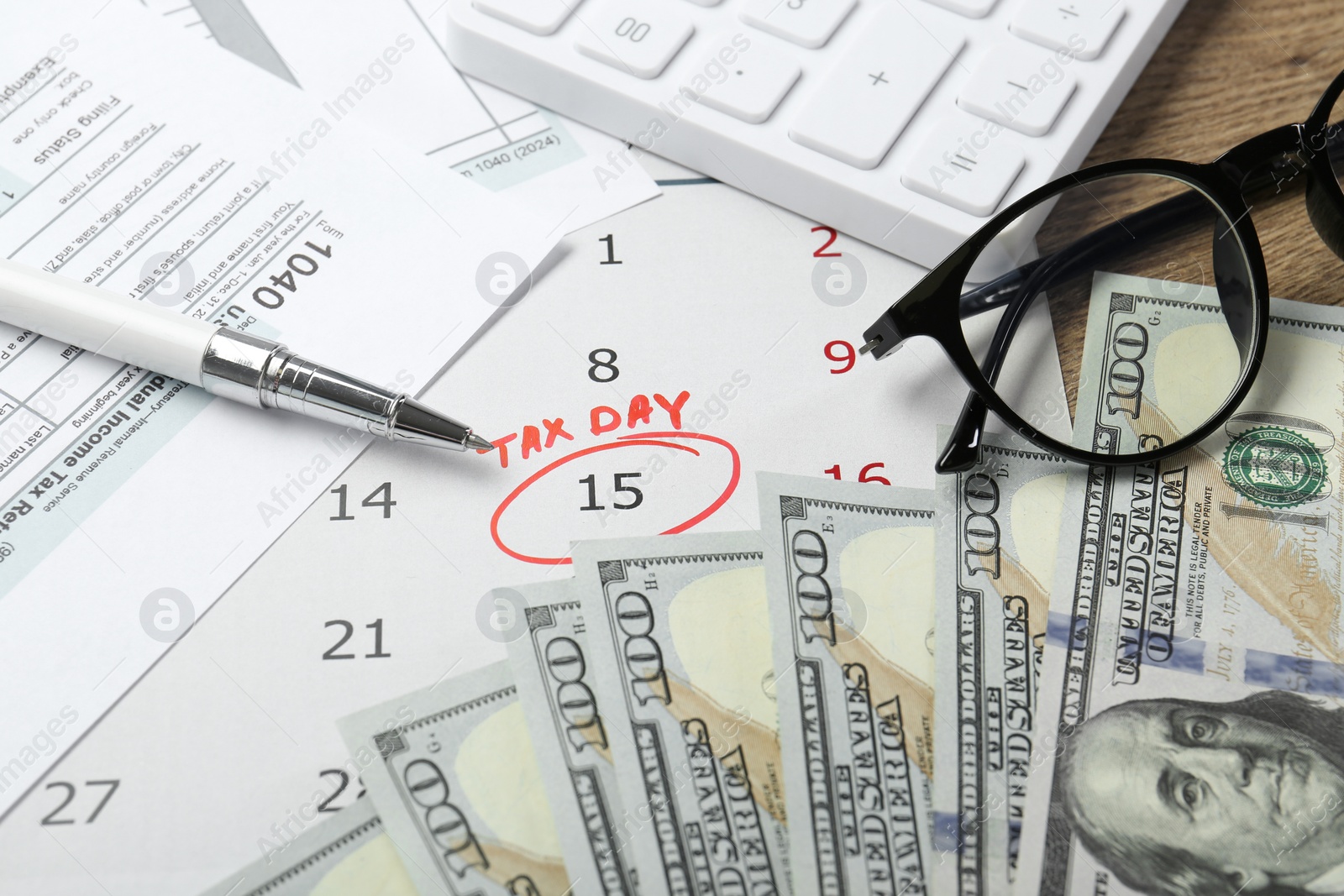 Photo of Calendar with date reminder about tax day, documents, pen, money, glasses and calculator on wooden table, closeup