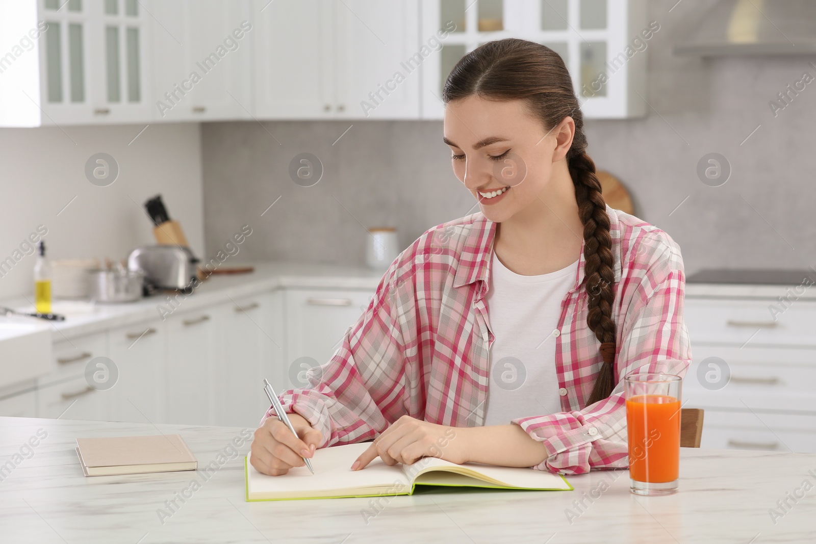 Photo of Beautiful young woman writing in notebook at white marble table indoors