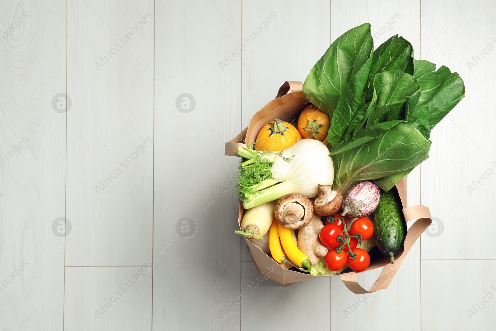 Photo of Paper bag full of fresh vegetables on light background, top view. Space for text