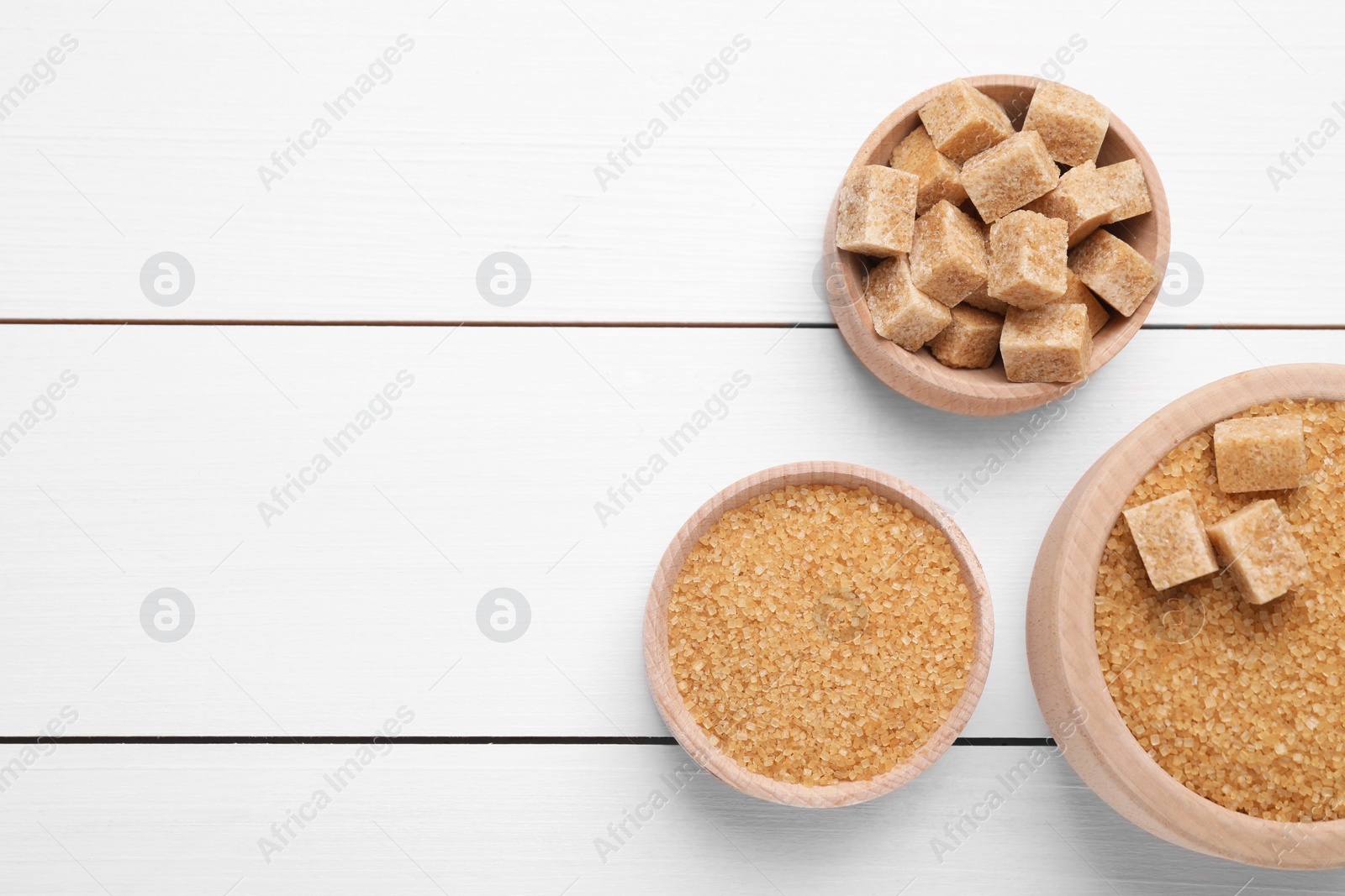 Photo of Different types of brown sugar in bowls on white wooden table, flat lay. Space for text